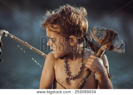 Angry Caveman, Manly Boy With Stone Axe And Bow Hunting Near River. Prehistoric Tribal Boy Outdoors 