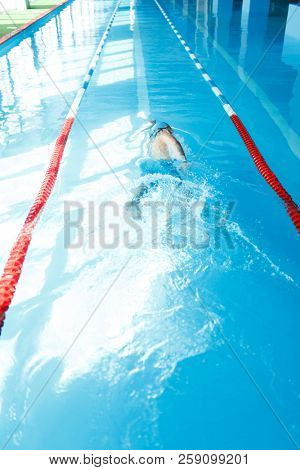 Photo of young sporty man in blue cap swimming on back in swimming pool