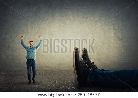 A Happy Businessman With Arms Raised Up Celebrate Victory Against His Giant Boss Fallen Down. Office