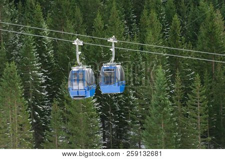 Two Cable Cars, That Go In Opposite Ways, Meet Over The Snowy Evergreen Fir Forest, In The Alps Moun