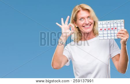 Middle age blonde woman holding menstruation calendar ver isolated background doing ok sign with fingers, excellent symbol