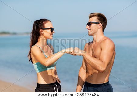 fitness, sport and lifestyle concept - happy couple in sports clothes and sunglasses on beach making fist bump gesture