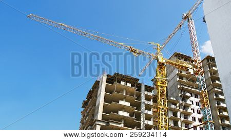 Two Tower Cranes And Two Buildings Under Construction Against The Blue Sky. Construction Site.