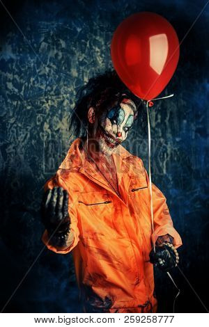 Sinister clown man stained in blood holding a balloon. Male zombie clown. Halloween. Horror.