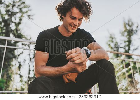 Happy Smiling Young Male Wears Black T-shirt And Wears Wirstwatch On The Street. Cheerful Man Posing