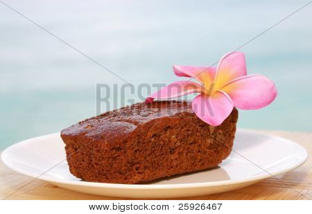 traditionel hawaiiansk bananbrød med en hot pink plumeria blomst på en hvid plade uden for med den 