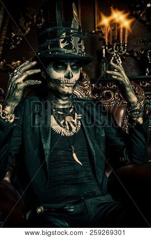 Halloween. A man with a skull makeup dressed in a tail-coat and a top-hat is in the old castle. Baron Saturday. Baron Samedi. Dia de los muertos. Day of The Dead. Old vintage interior.
