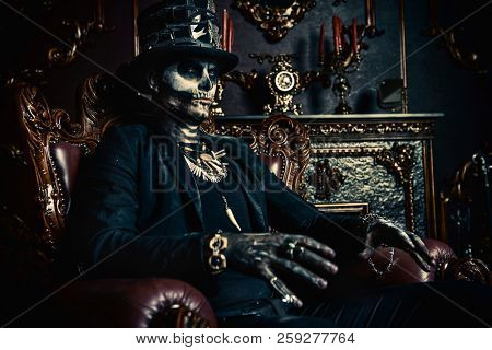 Halloween. A man with a skull makeup dressed in a tail-coat and a top-hat is in the old castle. Baron Saturday. Baron Samedi. Dia de los muertos. Day of The Dead. Old vintage interior.