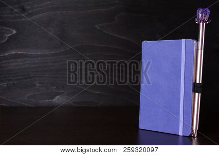 Purple Notepad With An Attached Pen On The Table On A Black Woodenl Background