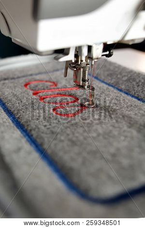 Closeup On Grey Felt With Red Lettering Stitched By A Modern Computerised Sewing Machine With Embroi
