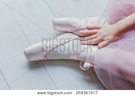 Hands Of Ballerina In Pink Tutu Skirt Puts On Pointe Shoes On Leg In White Light Hall. Young Classic