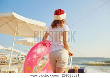 A Girl In A Santa Claus Hat With A Suitcase On The Beach On Chri