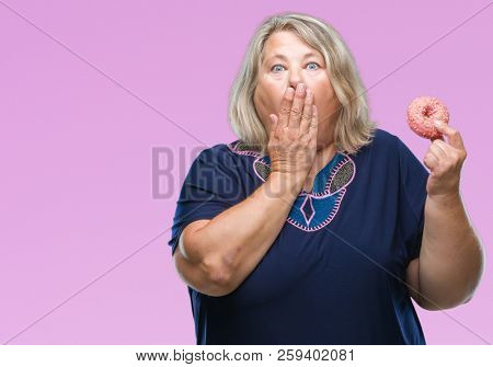 Senior plus size caucasian woman eating sugar donut over isolated background pointing with finger to the camera and to you, hand sign, positive and confident gesture from the front