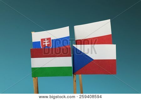 A Visegrad Four. Czech Republic, Poland, Hungaria, Slovakia. Flags On Wooden Stick. Blue Background