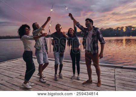 Creating Happy Memories. Full Length Of Young People In Casual Wear Smiling And Holding Sparkers Whi