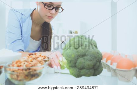 Portrait of female standing near open fridge full of healthy food, vegetables and fruits. Portrait of female
