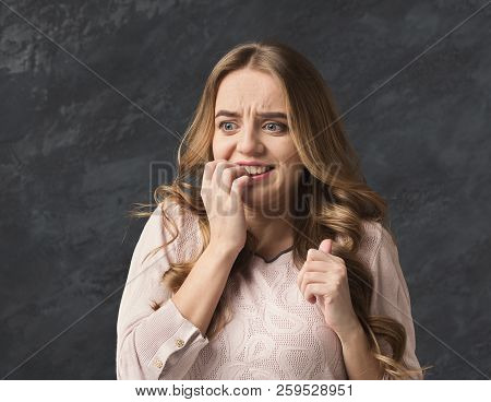 Young Nervous Girl Biting Her Nails, Worried Of Making Mistake, Black Studio Background
