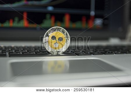 Golden And Silver Ripple Coin On A Black Keyboard Of Silver Laptop And Diagram Chart Graph On A Scre