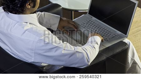 Mideastern Man Using Laptop At Office, With A Cup Of Cofee And Documents On The Side Table