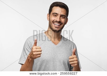 Young Laughing Man Isolated On Grey Background Showing Thumb Sup With Positive Emotions And Happines