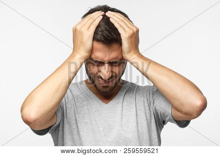 Young Man Isolated On Gray Background, Showing How Much His Head Hurts, Experiencing Pain, Looking M