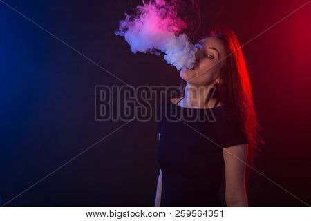 Portrait Of Asian Woman Smoking Vape Or E-cigarette In Neon Light At Black Background.