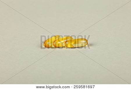 Close Up Three Yellow Omega 3 Vitamins And Essential Fish Oils Gel Cap Pills Over Grey Background Wi