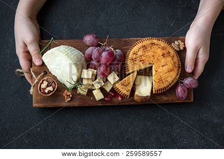 Cheese Platter With Assorted Cheeses, Grapes, Nuts And Hands Of Cheese Maker On Black Background. It