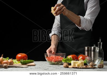 The Chef Prepares A Salad, Pours Lemon Juice On A Dark Background With An Empty Space For Writing