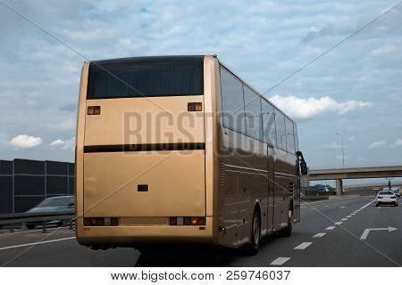Gold Intercity Bus Is Driving Along The Road. Back View. Sunny Day. The Sky With Clouds.