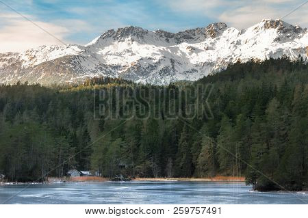 Blue Frozen Lake Surrounded By Evergreen Fir Forest And The Snowy  Alps Mountains, Near Biberwier Vi