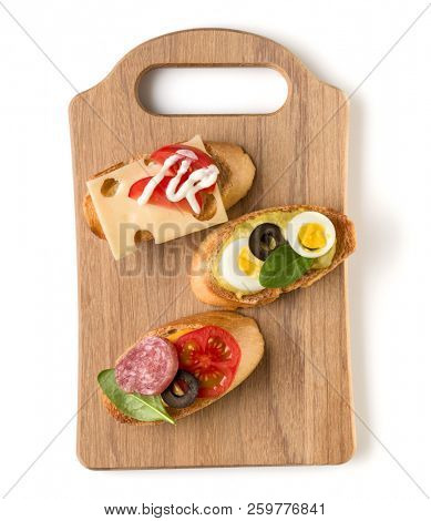 Open faced sandwich canape or crostini on a wooden serving board isolated on white background closeup. Top view.