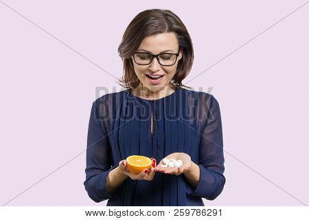 Woman Holds Natural Vitamin-orange In One Hand And Synthetic Vitamin C In The Other. Makes A Choice.