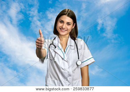 Pretty Doctor Geturing Thumb Up. Happy Smiling Medical Doctor With Stethoscope Showing Thumb Up On S
