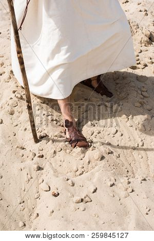 Cropped Image Of Jesus In Robe And Sandals Walking In Desert With Wooden Staff