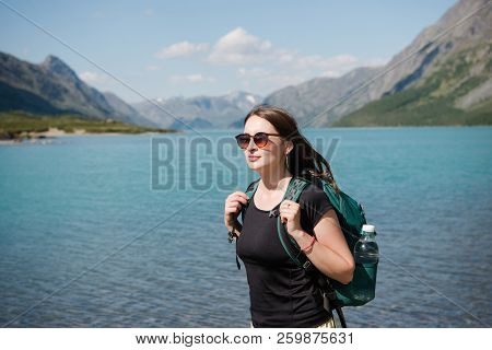 Beautiful Young Woman In Sunglasses With Backpack Standing Near Majestic Gjende Lake, Besseggen Ridg