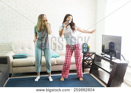 Young Female Roommates Singing And Dancing During Karaoke Party At Home