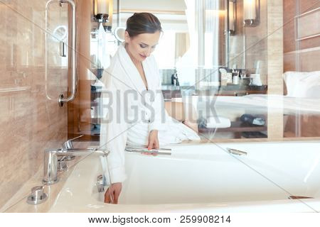 Woman in luxurious hotel bathroom letting water in the bathtub in animation of a relaxing experience 