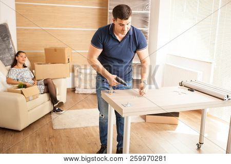 Smiling Man Putting Together Self Assembly Furniture In New Home.