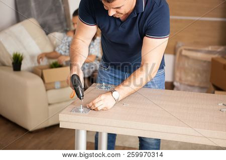 Man Is Working With Furniture Assembly Using Electric Screwdriver In New House.