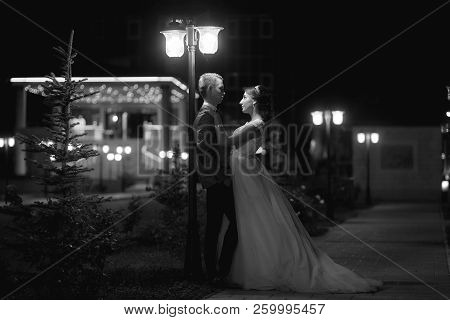 The Bride And Groom Stand On The Beautiful Porch Of The Hotel At Night