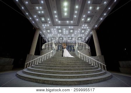 The Bride And Groom Stand On The Beautiful Porch Of The Hotel At Night