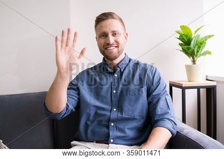 Portrait Of A Happy Young Man Waving Hand At Home
