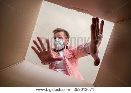 Man In A Medical Mask Unboxing Inside View A Delivered Box, Shows A Stop Gesture With Hands Afraid O