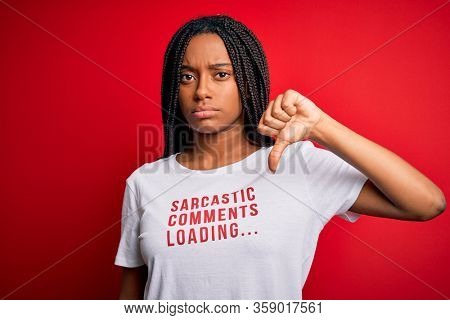 Young african american woman wearing sarcasm coments text on t-shirt over red background with angry face, negative sign showing dislike with thumbs down, rejection concept