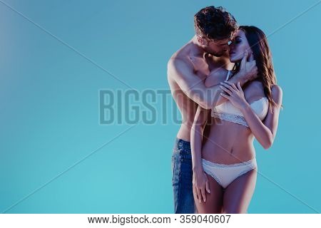 Shirtless Man Embracing And Kissing Sexy Girl In White Lingerie Isolated On Blue