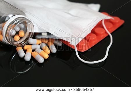 Pills And Capsules In Bottle With Medical Face Mask On Dark Glass Table. Protection And Profilactic 
