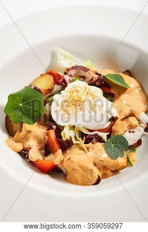 Salad in white bowl. Sliced octopus and fried potato. Served cut ingredients with mayonnaise, tomato spicy ajika and smoked pepper homemade sauce. Restaurant food portion in plate close up