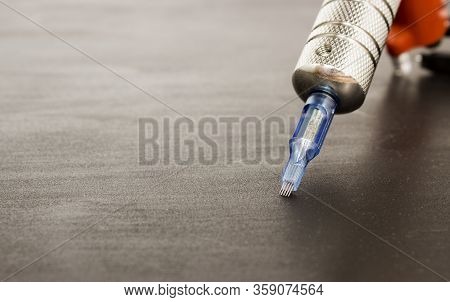 Part Of A Rotary Tattoo Machine With A Needle In Hand In A Black Glove On A Black Background. Side V