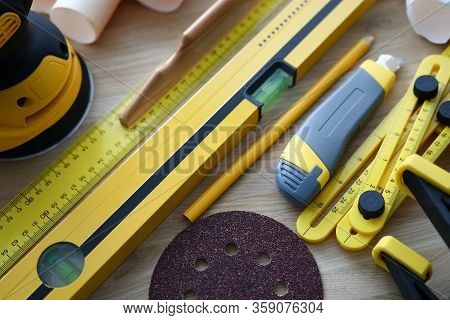 Close-up Of Level Ruler Pencil And Box Cutter On Wooden Table. Yellow Sander For Renovation Works. R